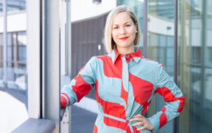 Hanna Sarkkinen seisoo värikkäässä mekossa ja katsoo kameraan.